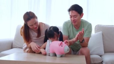 Mutlu Asyalı aile babası, anne ve kızı koltukta oturmuş para biriktirirken aynı zamanda bankaya para bırakıyor. Anne, baba ve çocuk depozitosu ve bütçe, yaşam tarzı kavramı..