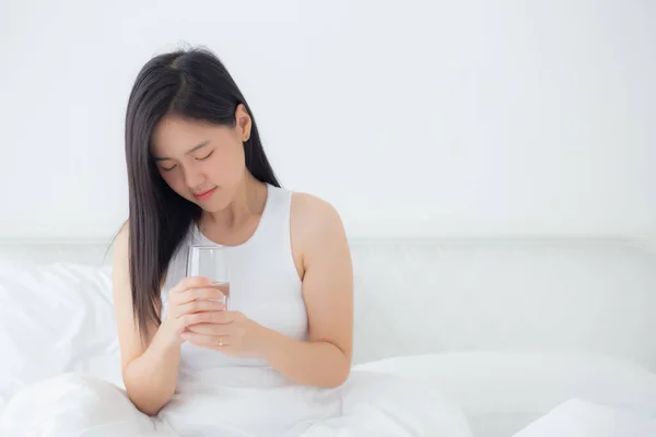 美しい若いアジアの女性のベッドの上にガラスの水を保持し 自宅でベッドルームで午前中に飲んで座って 健康と栄養のための女性の飲料ミネラル ライフスタイルの概念 — ストック写真
