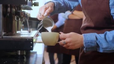 Kahve barmeninin kahve kapuçino ya da latte hazırlarken kahve fincanına süt koyduğu yakın plan genç Asyalı kadın kahve fincanı, küçük işletme ya da KOBİ 'de fincanla içki yapıyor..