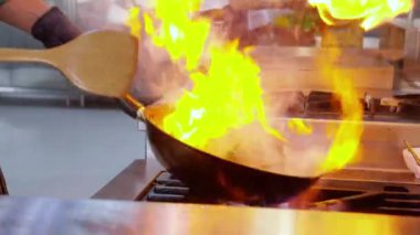 Şefin yakın elleri, sabah alevini, restoranda yanan tavayla, yemek ve besinle, yavaş çekimde yemek pişirme, aşçılık ve yemek tarifi ile karıştırıyor..