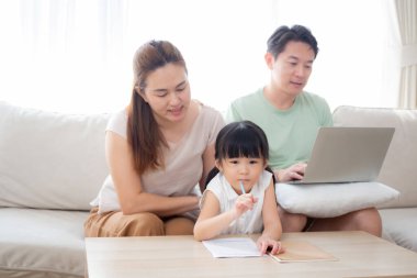 Mutlu bir aile, kızıyla ev ödevi öğreten bir anne ve baba evdeki kanepede dizüstü bilgisayarla çalışan bir anne, çocuklarla ilgili okul ödevlerini, yaşam tarzlarını ve eğitimi anlatıyor..