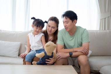 Mutlu Asyalı aile babası, anne ve kızı evdeki oturma odasında koltukta oturuyor, mutlu baba, anne ve çocuk birlikte kanepede rahatça oturuyor, yaşam tarzları kavramı..
