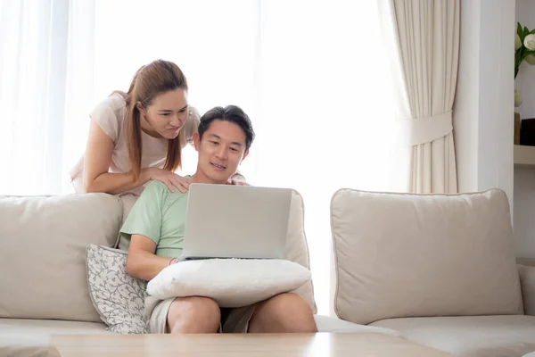 自宅のリビングルームでソファの上でリラックスしてレジャーとソーシャルメディアやビデオを探してラップトップコンピュータを使用して若いアジアのカップル インターネットへのラップトップを見て男と女 ライフスタイルの概念 — ストック写真