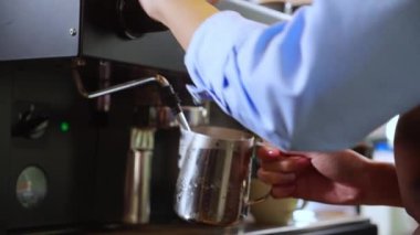 Kahve dükkanındaki sürahide kahve yapmak için buharlı süt ya da köpük hazırlayan baristanın yakın çekim elleri, kapuçino ya da makineli latte yapan Asyalı genç kadın, küçük işletme ya da KME.