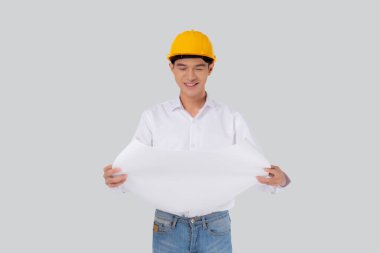 Portrait young asian man is engineer wearing helmet holding and looking blueprint with confident isolated on white background, handsome male is architect or contractor, worker or labor concept.