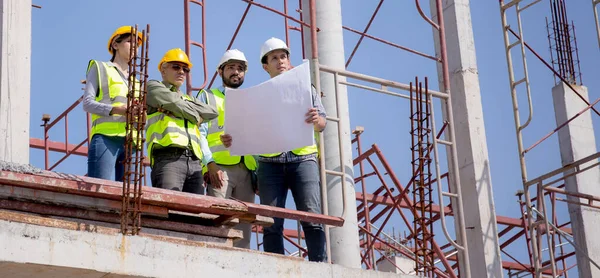 Bir grup müteahhit ve mimar ustabaşıyla birlikte proje planlama projesini işçilere ve proje, inşaat alanı, geliştirme ve yapıya bakmaları için planlama sahasından bahsediyorlar..