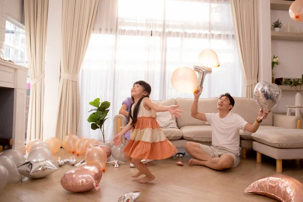 Happy asian family father and mother and daughter play balloon with enjoy and fun while celebration in living room at home, dad and mom and kid relax and recreation, lifestyles and relation concept.