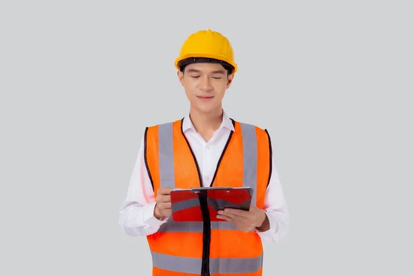 ヘルメットを着て肖像若いアジアのエンジニアの男性は 産業概念のための文書やクリップボード隔離された白い背景 建築家や請負業者のチェックと診断に関するレポートを見て — ストック写真