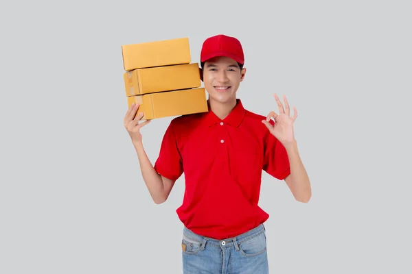 身穿制服的亚洲年轻人站着 头戴红帽 提着箱子 摆出一副孤立的白色背景 员工持货物 快递和送货 运输和服务 物流和货运 — 图库照片