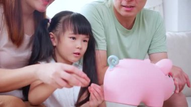 Mutlu Asyalı aile babası, anne ve kızı koltukta oturmuş para biriktirirken aynı zamanda bankaya para bırakıyor. Anne, baba ve çocuk depozitosu ve bütçe, yaşam tarzı kavramı..