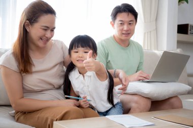 Mutlu bir aile, kızıyla ev ödevi öğreten bir anne ve baba evdeki kanepede dizüstü bilgisayarla çalışan bir anne, çocuklarla ilgili okul ödevlerini, yaşam tarzlarını ve eğitimi anlatıyor..