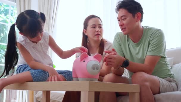 幸せなアジアの家族の父と母と娘は お部屋 お母さんとお父さんと子供の預金と予算 ライフスタイルの概念で貯金をしながらソファ計画ファイナンスに座っている — ストック動画