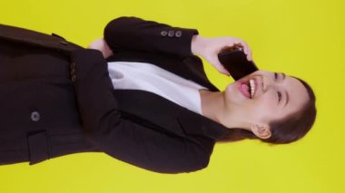 Takım elbiseli genç Asyalı iş kadını sarı arka planda izole edilmiş akıllı telefondan konuşuyor, iş kadını akıllı telefondan konuşuyor, cep telefonu tutan kadın, iletişim konsepti.