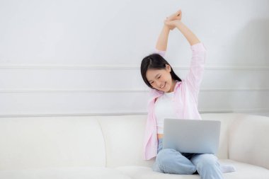 Beautiful young asian businesswoman sitting on sofa and working from home and break while stretch arm for relax in living room at home, woman is freelance working on laptop computer, business concept.