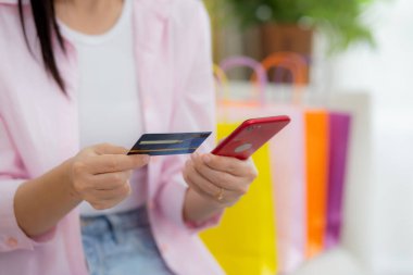 Hands of woman sitting on sofa using smart phone shopping online with credit card while paper bag on couch, happy female paying with transaction financial, purchase and payment, business concept.