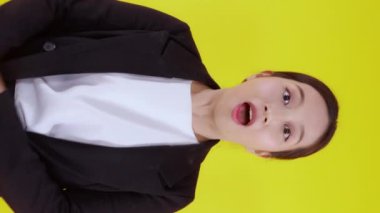 Sarı arka planda mutlu ve başarılı bir şekilde duran takım elbiseli güzel iş kadını, genç Asyalı iş kadını yönetici ya da yönetici gülümsemesi, zafer için heyecanlı ve sürpriz..