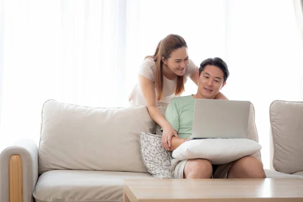 自宅のリビングルームでソファの上でリラックスしてレジャーとソーシャルメディアやビデオを探してラップトップコンピュータを使用して若いアジアのカップル インターネットへのラップトップを見て男と女 ライフスタイルの概念 — ストック写真