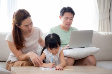 Mutlu bir aile, kızıyla ev ödevi öğreten bir anne ve baba evdeki kanepede dizüstü bilgisayarla çalışan bir anne, çocuklarla ilgili okul ödevlerini, yaşam tarzlarını ve eğitimi anlatıyor..