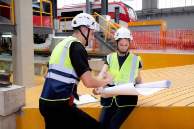 Genç Kafkasyalı mühendis ve kadın ya da işçi planları arıyor ve istasyon, ulaşım ve altyapı planlaması için elektrik trenini kontrol ediyor..