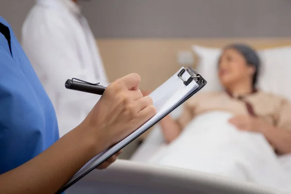 간호사는 병원에서 환자와 클립보드 위에서 보고서를 작성하고 악화를 검사하고 문서를 — 스톡 사진