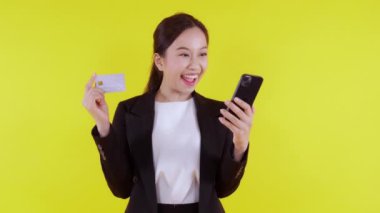 Genç Asyalı iş kadını portresi kredi kartı tutuyor ve internetten alışveriş yapmak için akıllı telefon arıyor sarı arka plan, banka kartı ve akıllı telefon arayan iş kadını, finansal konsept.