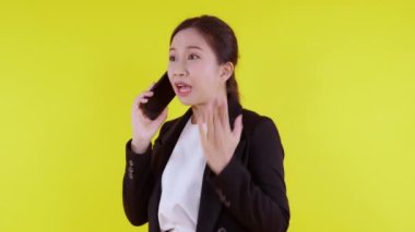 Asyalı genç iş kadınının portresi. Sinirli bir şekilde sarı arka planda izole edilmiş akıllı telefondan arıyor. İş kadını öfke, iletişim ve duygu konseptiyle bağırıyor ve strese giriyor..
