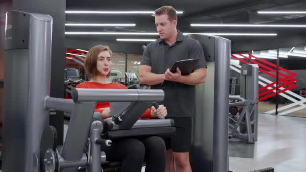 Trener Mężczyzna Prowadzenie Treningu Mięśni Nóg Rozciągnąć Urządzenia Kobietą Siłowni — Wideo stockowe