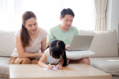 Mutlu bir aile, kızıyla ev ödevi öğreten bir anne ve baba evdeki kanepede dizüstü bilgisayarla çalışan bir anne, çocuklarla ilgili okul ödevlerini, yaşam tarzlarını ve eğitimi anlatıyor..