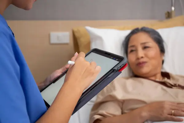 stock image Closeup hands nurse writing report document about prescribe medical and health care on tablet while check and diagnostic with elderly patient in hospital, examining disease, senior unwell.