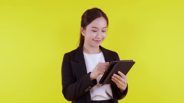 黄色の背景に隔離されたインターネットにタブレットコンピュータを使用して立ってスーツ姿の若いアジアの実業家の肖像画 ビジネス女性のタッチスクリーンデジタルタブレット成功し 通信コンセプト — ストック動画