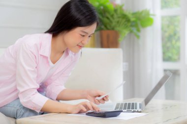 Genç Asyalı kadın evde hesap makinesiyle finans evini hesaplıyor, kız tasarruf ve planlama masrafları, borç ve kredi, vergi ve muhasebe, iş ve mali konsebe için faturaları kontrol ediyor.