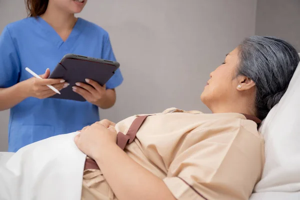 护士在对住院老年病人进行解释 检查和诊断时 在平板电脑上填写有关医疗和保健的报告文件 检查疾病 在护士来访时检查老年病人 — 图库照片