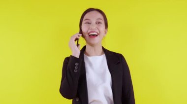 Takım elbiseli genç Asyalı iş kadını sarı arka planda izole edilmiş akıllı telefondan konuşuyor, iş kadını akıllı telefondan konuşuyor, cep telefonu tutan kadın, iletişim konsepti.