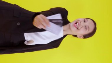 Güzel Asyalı genç iş kadınının portresi kredi kartı ya da alışveriş için kredi kartı ya da banka kartı taşıyor ve sarı arka planda finansla işlem yapıyor, iş kadını ATM, finans konsepti gösteriyor.