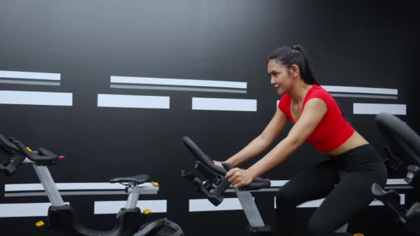 フィットネスジムクラブでのトレーニングのためのワークアウトトレーニングのための自転車マシンに乗る若いアジアの女性 健康と減量のための動機と濃度と運動のための女性のサイクリング スポーツと医療 — ストック動画