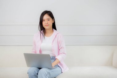 Genç Asyalı iş kadını evde dizüstü bilgisayarla çalışıyor oturma odasındaki kanepede internete bağlanıyor, defter kullanan serbest bir kız rahat ve rahat bir şekilde kanepede oturuyor, yaşam tarzı kavramı..