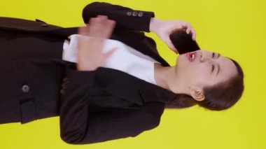 Asyalı genç iş kadınının portresi. Sinirli bir şekilde sarı arka planda izole edilmiş akıllı telefondan arıyor. İş kadını öfke, iletişim ve duygu konseptiyle bağırıyor ve strese giriyor..