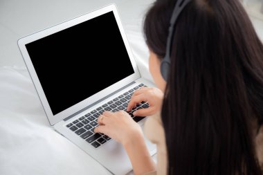 Young asian woman work from home with laptop computer blank screen mockup, freelance is female using notebook with empty, girl typing keyboard and wearing headset, business and communication concept.
