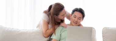 Genç Asyalı çift, sosyal medyayı veya videoyu izlemek için dizüstü bilgisayar kullanıyor. Evdeki oturma odasındaki kanepede rahatça oturuyor, kadın ve erkek bilgisayardan internete dizüstü bilgisayar izliyor, yaşam tarzı kavramı....