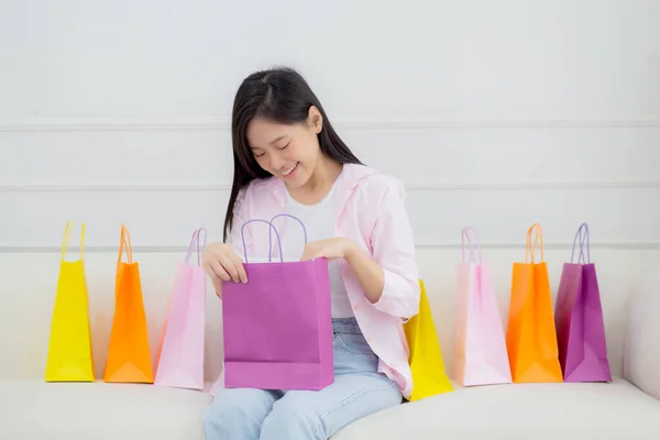 快乐的年轻亚洲女人坐在沙发上打开纸袋 带着信用卡在网上购物 女孩购物和打折的消费者兴奋 购物和生活方式的概念 — 图库照片