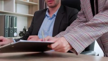 Genç Kafkasyalı işadamı, sekreterin ofiste imza atması için belge verirken dizüstü bilgisayar kullanıyor. İş kadını imzaya belge verirken, yönetici de defter üzerinde çalışıyor..