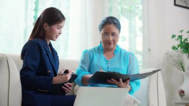 Ajans sigortası ya da sağlık ya da danışman genç Asyalı kadın ve yaşlı kadın oturma odasında anlaşma yapıyor ve belge imzalıyor, sağlık, iş ve sigorta için plan yapıyor.