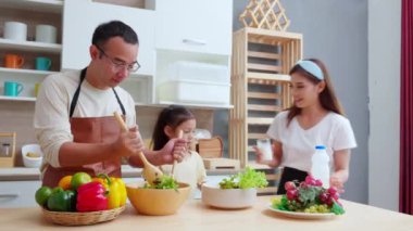 Baba, anne ve kız birlikte salata hazırlarken, evde süt içen kız, baba, anne ve çocuk salatayla kahvaltı hazırlarken Asyalı mutlu bir aile..