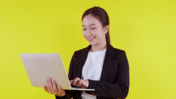 黄色の背景にラップトップコンピュータ上でインターネットに仕事を立って肖像若いアジアのビジネス女性 自信を持ってスーツのビジネス女性とノートブックを使用して マーケティングと通信 — ストック動画