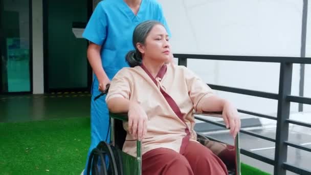 在医院花园照料坐在轮椅上的老年病人时 照料者亚洲妇女行走 在医生或护士的帮助下进行高级治疗和康复治疗 医学概念 — 图库视频影像