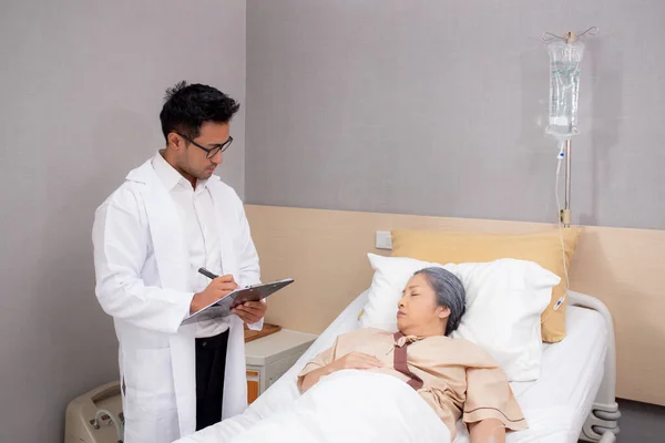Doctor checkup and diagnostic with patient elderly woman for prescription or planning rehabilitation at hospital, physician talking with patient and writing document, medical and insurance concept.