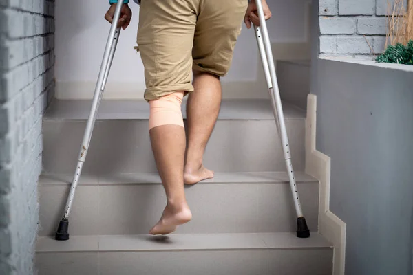 Closeup leg young asian man walking on stair with crutch at home, close-up man walking while bandage with leg, rear view, medical and lifestyle concept.
