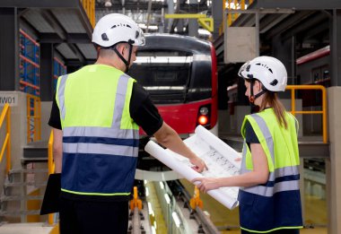 Genç Kafkasyalı mühendis ve kadın ya da işçi planları arıyor ve istasyon, ulaşım ve altyapı planlaması için elektrik trenini kontrol ediyor..