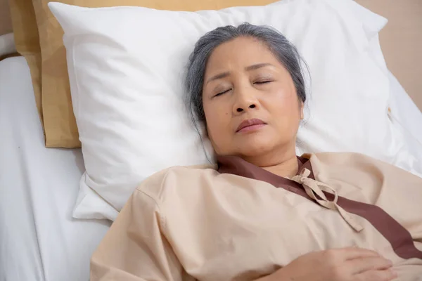 Asian elderly woman asleep on bed with surveillance in hospital ward, patient senior unconscious lying on bed, elder ill while relax at clinic, ailment and treatment, medical and insurance concept.