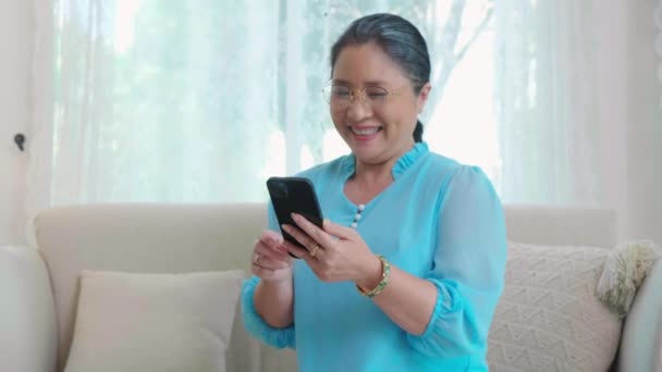 Azjatyckie Starsza Kobieta Pomocą Smartfona Mediów Społecznościowych Online Siedzi Kanapie — Wideo stockowe